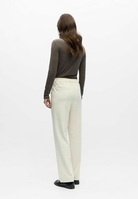 Bukser i kremfarge med vide ben, myk tekstur og elastisk midjebånd. Modellen har på seg en tettsittende, brun topp med lange ermer.