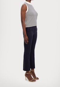 Sleeveless striped top in cream and navy, paired with tailored navy pants and tan strappy high-heeled sandals. Focus on clean lines and fit.