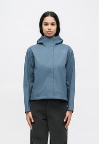 Αδιάβροχο, με κουκούλα μπουφάν σε ανοιχτό μπλε, με φερμουάρ μπροστά, ανοιχτά μανίκια και ελάχιστη επωνυμία. Λεία υφή, κοντό σχέδιο.