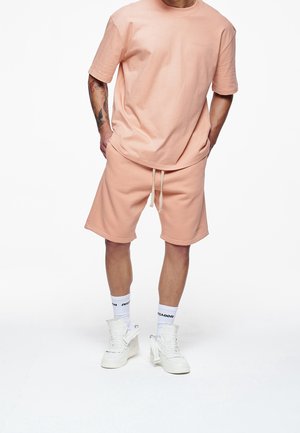 Peachfärgad bomulls t-shirt och shorts-set med en avslappnad passform. Anmärkningsvärda detaljer inkluderar dragsko i midjan och vita sneakers.
