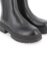 Botas de cuero negro hasta el tobillo con paneles laterales elásticos, suelas de goma gruesas y un patrón de relieve prominente. Textura suave y diseño de punta redonda.