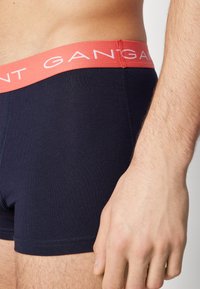 Navy bomull boxershorts med korallfarget elastisk midjebånd som har hvit logo tekst, glatt tekstur, og synlig sømdetalj på kantene.
