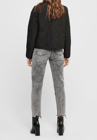 Sort quiltet jakke med en cropped design, parret med blege grå jeans med en frynset kant og sorte ankelstøvler.