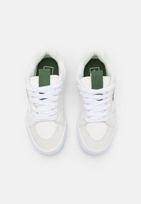 Baskets en toile blanches avec des accents en daim, des lacets blancs et un tirant au talon vert. Elles présentent un dessus texturé et une semelle en caoutchouc plate.