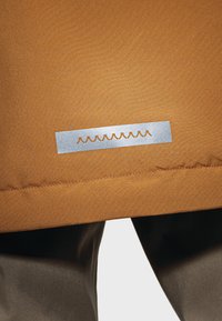 Brown outer fabric with a smooth texture, featuring a silver rectangular tag embossed with a wavy line pattern.