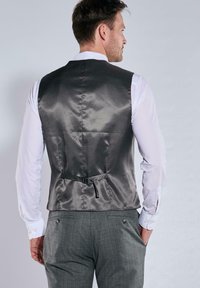 Graue Satinweste mit glatter Textur, Rückengurt zur Anpassung und einem weißen Hemd darunter. Die maßgeschneiderte Passform betont die Form.