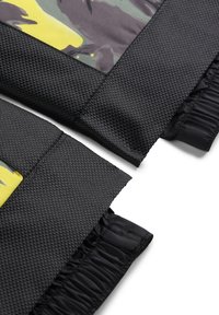 Zwart gestructureerd stof met een honingraat patroon en gladde accenten, met een geel en groen camouflageontwerp aan de bovenrand.