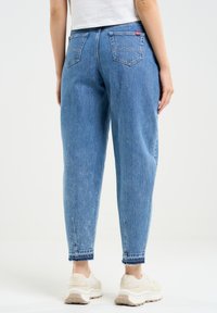 Helle blaue Denim-Jeans mit lockerer Passform, ausgestattet mit einem Bund, zwei Gesäßtaschen und ausgefransten Säumen. Kombiniert mit beigen Turnschuhen.