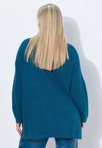 Übergroßer, türkisfarbener Strickpullover mit strukturiertem Muster und gesenkten Schultern, der eine entspannte Passform und lange Ärmel aufweist.