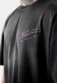 Black cotton t-shirt featuring long sleeves, a round neckline, and a pink embroidered logo on the left chest. Soft texture, relaxed fit.