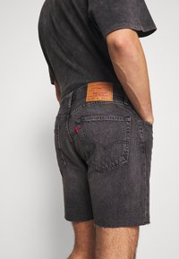 Black denim shorts featuring a frayed hem, back pockets, and a visible leather patch with branding at the waistband.