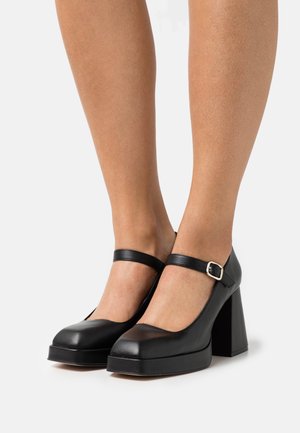 Zwarte Mary Jane hakken met vierkante neus, stevige hak en enkelbandje. Gemaakt van glad leer met een lichte glans en een zilverkleurige gesp.