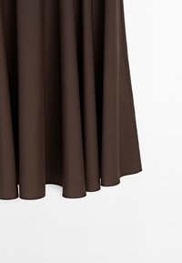 Mørkebrun nederdel i stof med bløde folder mod en hvid baggrund, der viser tøjets bevægelse og tekstur.