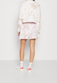 Cropped jacket and matching skirt with a pastel floral pattern in pink, beige, and white. Model wears white shoes with red accents.