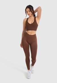 Braun geripptes Sport-BH und hochgeschnittene Leggings mit tailliertem Design. Getragen mit weißen Sportschuhen. Glatte Textur, schlichte Linien.