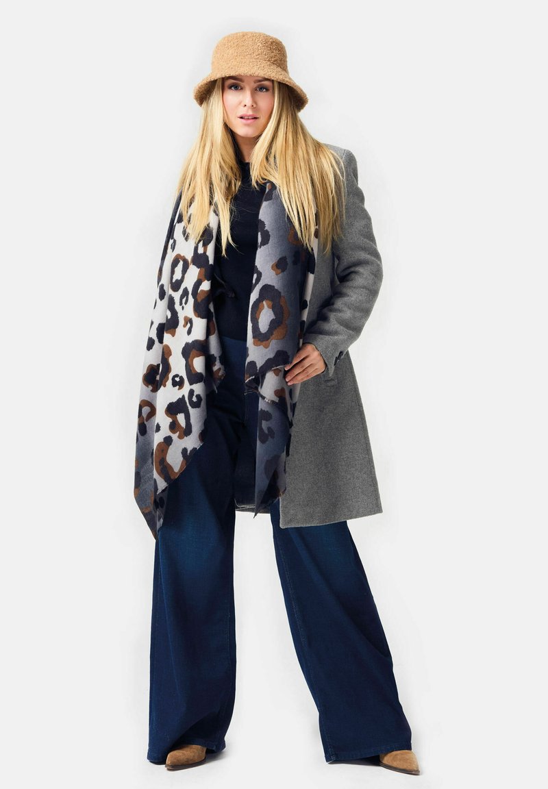 Gray wool coat over a black top, paired with wide-leg dark jeans and a leopard-patterned scarf. Tan bucket hat and brown shoes complete the look.