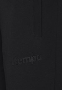 Schwarze Sweatpants aus weichem Stoff, mit einem strukturierten Bund und einem dezenten, erhabenen "Kempa"-Logo an der unteren Beinseite.