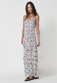 Robe maxi en tissu noir, blanc et rose à motifs. Dotée de couches volantes, de fines bretelles et d'une coupe décontractée. Associée à des sandales noires.