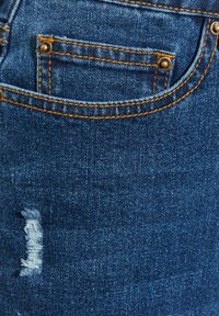 Granatowe dżinsy z kontrastowym pomarańczowym przeszyciem, małą kieszonką z przodu oraz przetarciem na nodze.