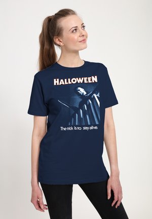 Ung kvinde med hestehale bærer en mørkeblå Halloween-t-shirt med en figur, der svinger en kniv, og teksten "Tricket er at overleve."