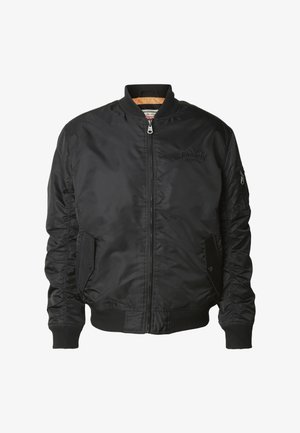 Svart bomberjakke med frontglidelås, ribbestrikket krage og mansjetter, to fremre klafflommer og en liten glidelåslomme på venstre erme.