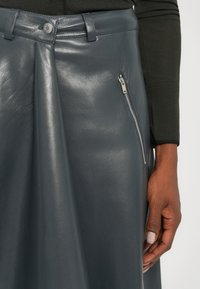 Gonna in pelle grigia con finitura texturizzata, una piega frontale, una tasca laterale con zip e chiusura a bottone.