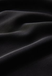 Tessuto nero con una texture liscia e leggermente lucida, caratterizzato da onde e pieghe sottili. Il materiale appare morbido e flessibile.