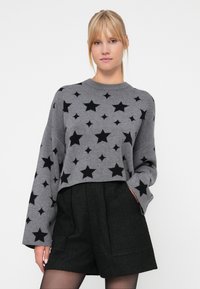 Grå cropped genser med stjernemønster i svart, lange ermer og rund hals, kombinert med strukturerte svarte shorts.