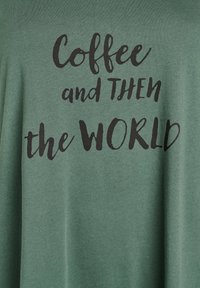 Green cotton t-shirt with a soft texture displaying the phrase "Coffee and THEN the WORLD" in bold black lettering.