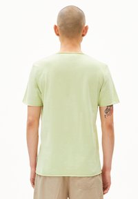 Hellgrünes Baumwoll-T-Shirt mit kurzen Ärmeln, rundem Ausschnitt und sichtbaren Nähten entlang der Kanten, kombiniert mit beige Hosen.