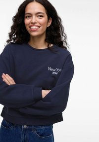 Tamsiai mėlynas džemperis su siuvinėtų "New York 1994" užrašu ant krūtinės. Turi apvalią iškirptę ir per dideles rankoves. Derinamas su džinsais.