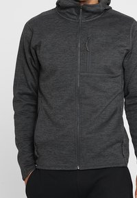 Gray fleece zip-up hoodie with a lined hood, front zipper, and a chest pocket. Features a textured finish and minimal branding.