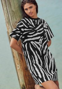 Robe t-shirt à rayures noires et blanches avec des manches courtes, présentant une coupe décontractée et une texture lisse, sur fond naturel.