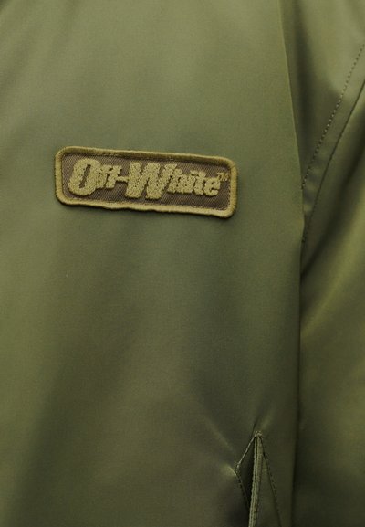 Πράσινο ύφασμα με ραμμένο ορθογώνιο σχέδιο που γράφει «Off-White» σε τόνους πράσινου που ταιριάζουν, σε ένα σακάκι ή ρούχο.