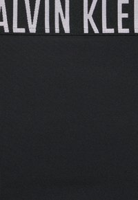 Tecido preto com uma textura suave, apresentando um logotipo branco bordado proeminente "CALVIN KLEIN" na cintura. Design simples e moderno.