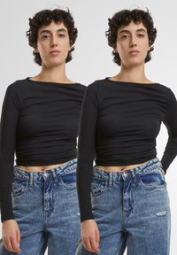 Fekete, hosszú ujjú crop top, hajónyakkivágással, magas derekú kék farmernadrággal párosítva, amelyen kopottas befejezés és enyhe kopás látható.