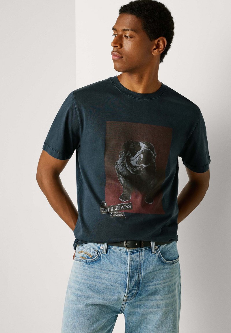 Camiseta de algodón azul marino con un gráfico de un perro sobre un fondo burdeos, cuello redondo y mangas cortas. Combinada con jeans azul claro.