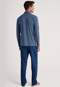 Blauw langemouwen patroon shirt met witte geometrische ontwerpen, gecombineerd met effen blauwe broek. De stof lijkt glad en lichtgewicht te zijn.