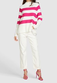 Pull bicolore rayé en blanc et rose vif, tricoté, avec poignets et ourlet côtelés. Associé à un jean blanc avec revers roulés et des sandales à talons roses.