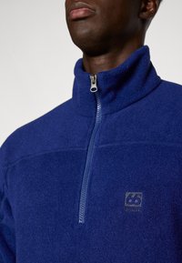 Marineblauwe fleece pullover met een hoge kraag en een kwart ritssluiting. Bevat een klein logo op de borst en een zachte, gestructureerde stof.