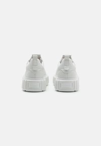 Baskets blanches avec une semelle épaisse, texture en cuir lisse et une languette au talon. Présente un logo accentué sur le talon.