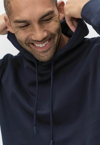 Marinblå hoodie i mjukt material, med dragsko i huven, framficka och diskret logotypdetalj på bröstet.