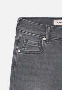 Jeans de denim cinza escuro com corte slim, design padrão de cinco bolsos e detalhes em metal no bolso frontal e na cintura.