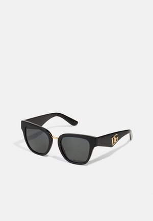 Óculos de sol pretos com uma armação geométrica, lentes cinzentas e um detalhe dourado na ponte. Apresenta um logótipo na lateral do cabo.