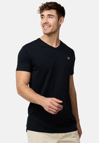 Camiseta de algodón negra con cuello en V, mangas cortas y un pequeño logo blanco en la parte izquierda del pecho. Textura suave y diseño ajustado.