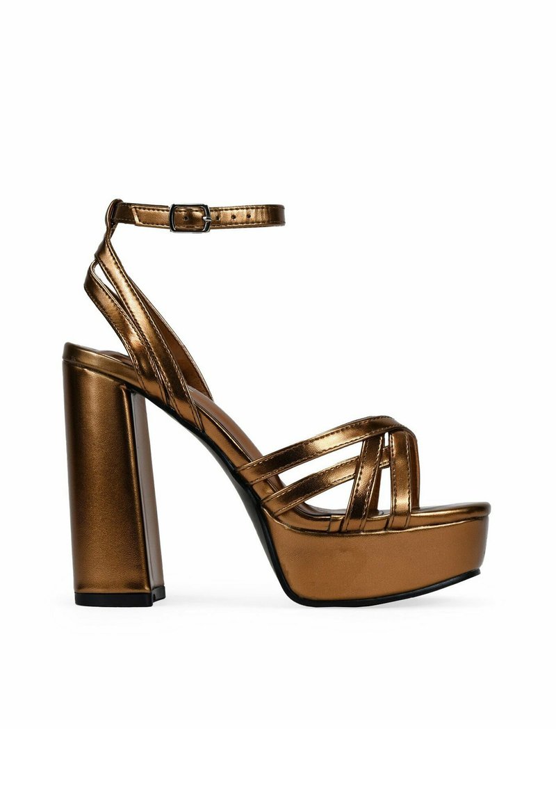 Talons compensés en bronze métallique avec un design à lanières, large talon bloc et bandeau à la cheville réglable. Texture lisse et finition brillante.