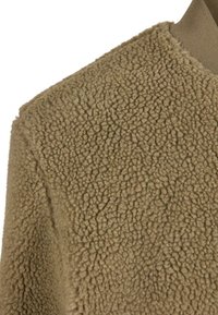 Fleece-stof i beige med en blød, tekstureret overflade og et let hævet, fluffy udseende. Enkel design uden yderligere detaljer.