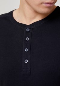 Černé žebrované triko henley s tříknoflíkovou légou, kulatým výstřihem a texturovanou tkaninou. Hladké knoflíky s jemným leskem.