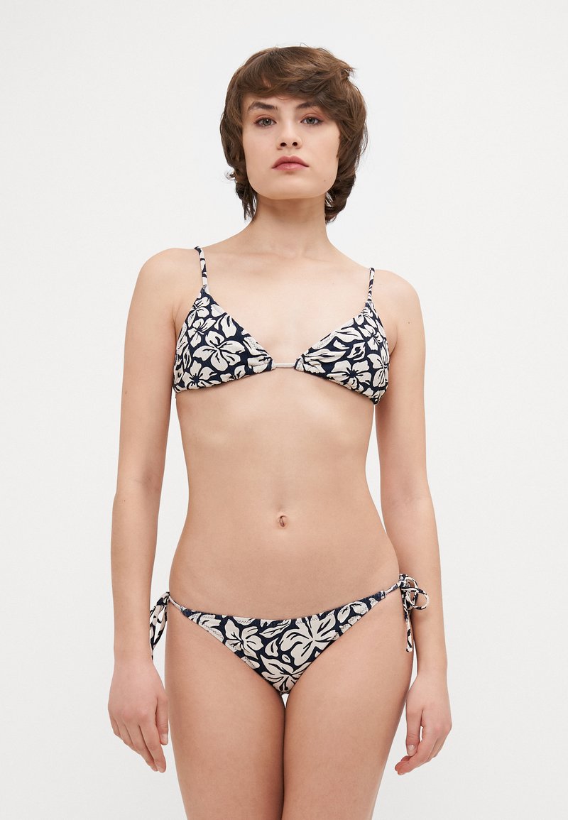 Két részes bikini, háromszög alakú melltartóval és kötéssel rendelkező alsó résszel. Tengerészszínű háttérrel, fehér virágmintával rendelkezik. Könnyű anyagból készült.