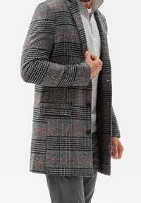 Gråternet frakke med orange detaljer, med en enknaps design, to knapper og en spids krave over en grå lynlåstop.